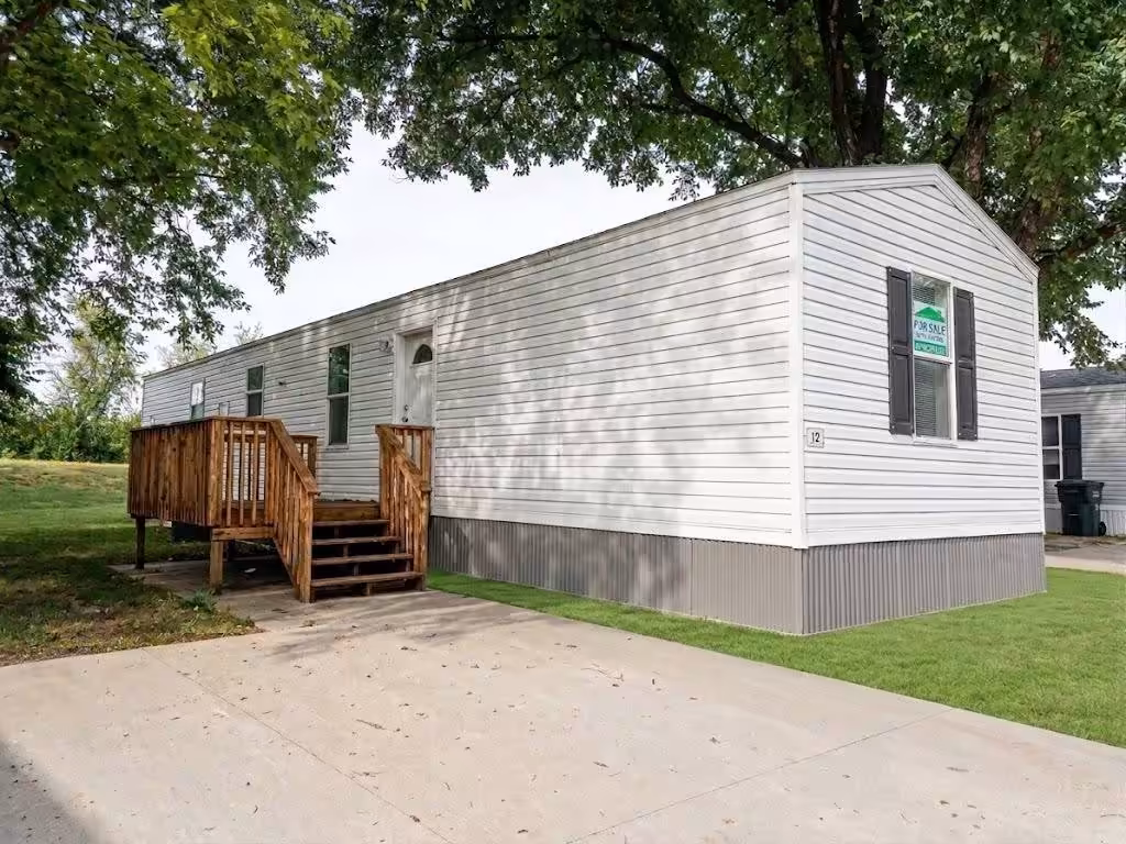 White mobile home with wooden deck and stairs under large tree, Palace sign in window.