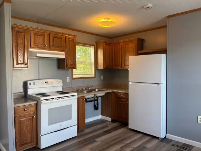 Kitchen with white stove and refrigerator, oak cabinets, sink under window, wood-look flooring.