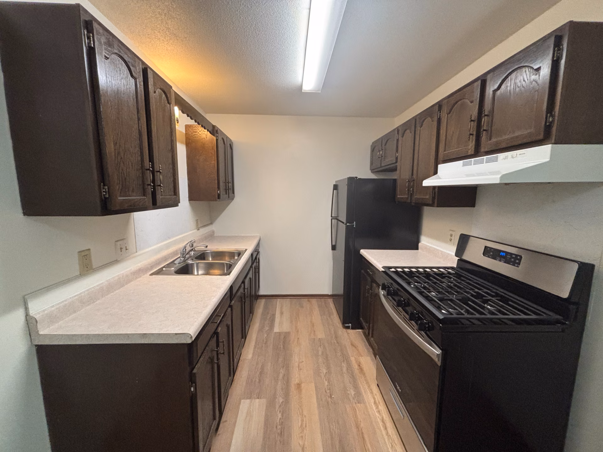 Kitchen with dark wood cabinets, white countertops, black fridge, gas stove, wood floors