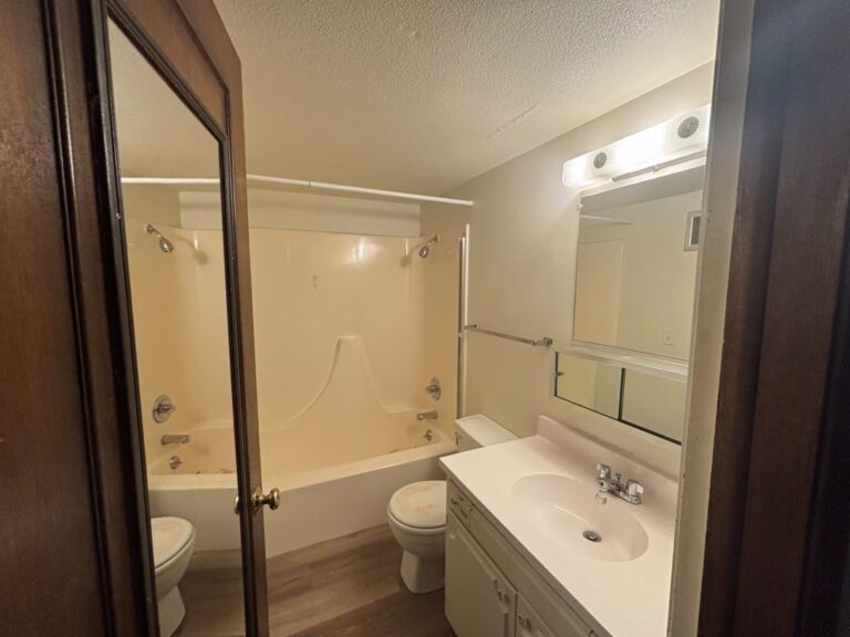 Bathroom with beige tub, toilet, and white sink vanity with mirror, viewed through an open door