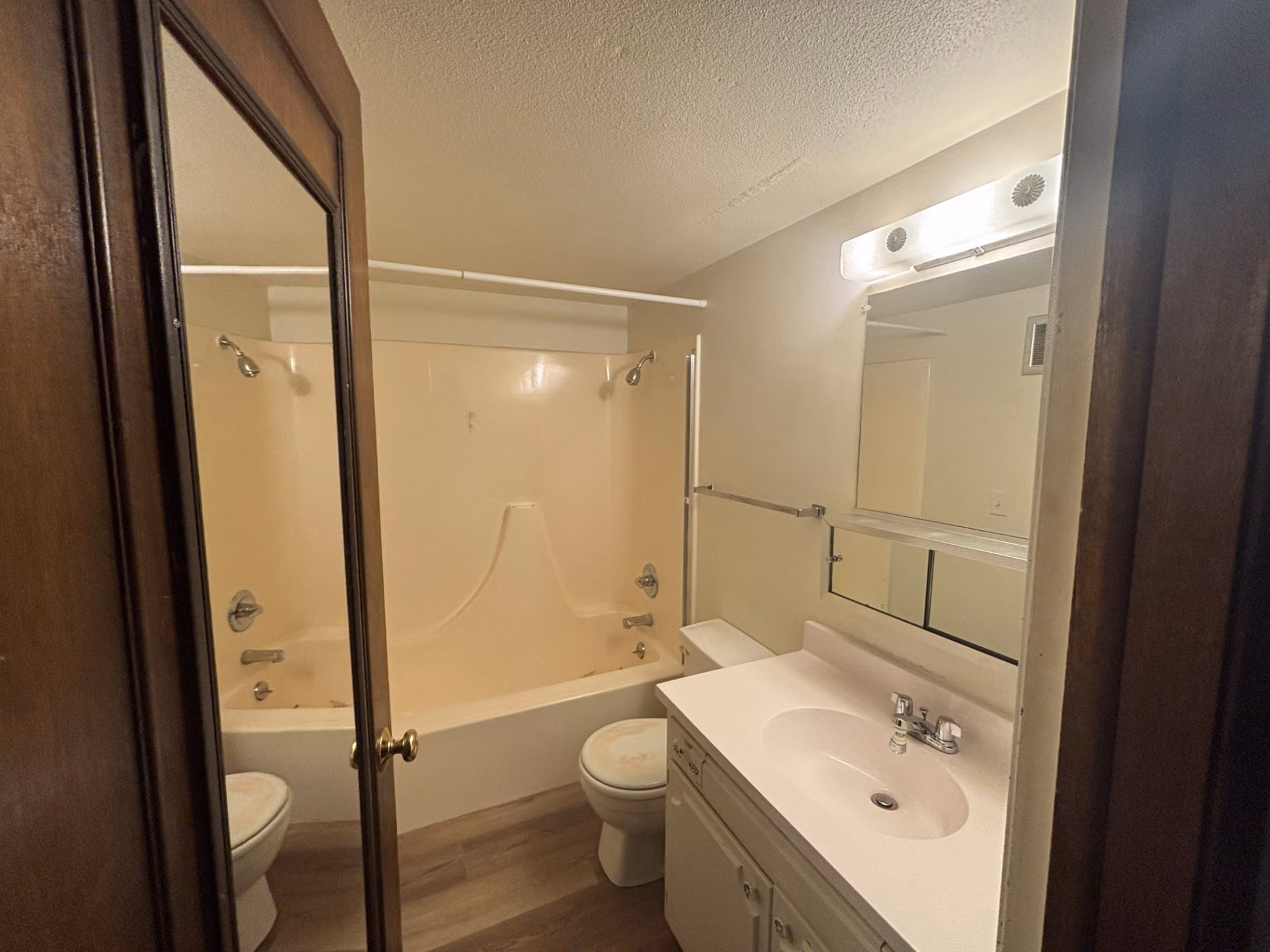 Bathroom with beige tub, toilet, and white sink vanity with mirror, viewed through an open door