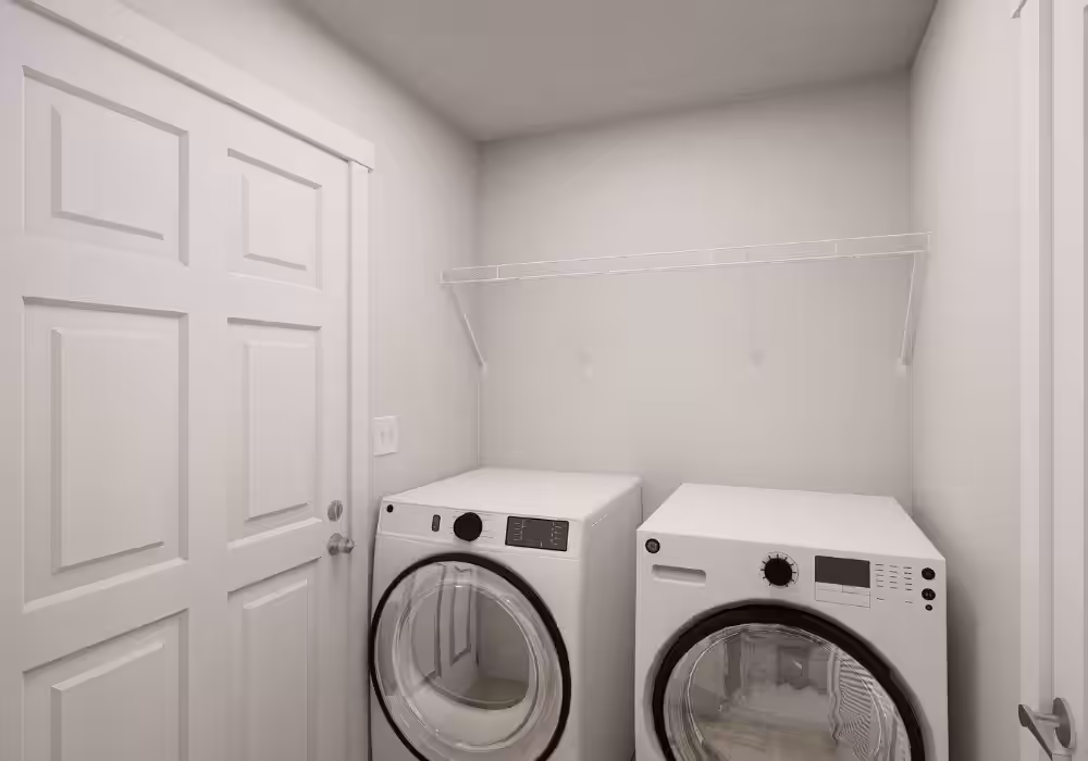 Laundry room with white GE washer and dryer beneath white shelf, beside white paneled door.