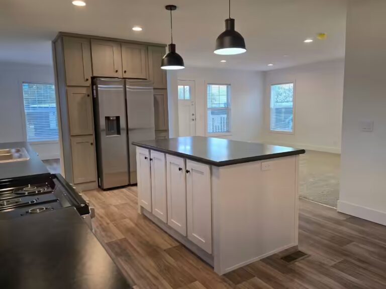 Modern kitchen with white island, pendant lights, gray cabinets, and stainless steel refrigerator