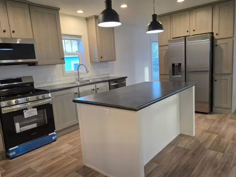 Kitchen with gray cabinets, black pendant lights, center island, and stainless steel appliances.