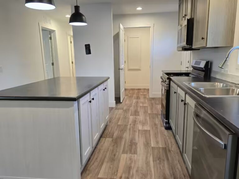 Kitchen with island, white cabinets, dark countertops, stainless appliances, and wood-look flooring