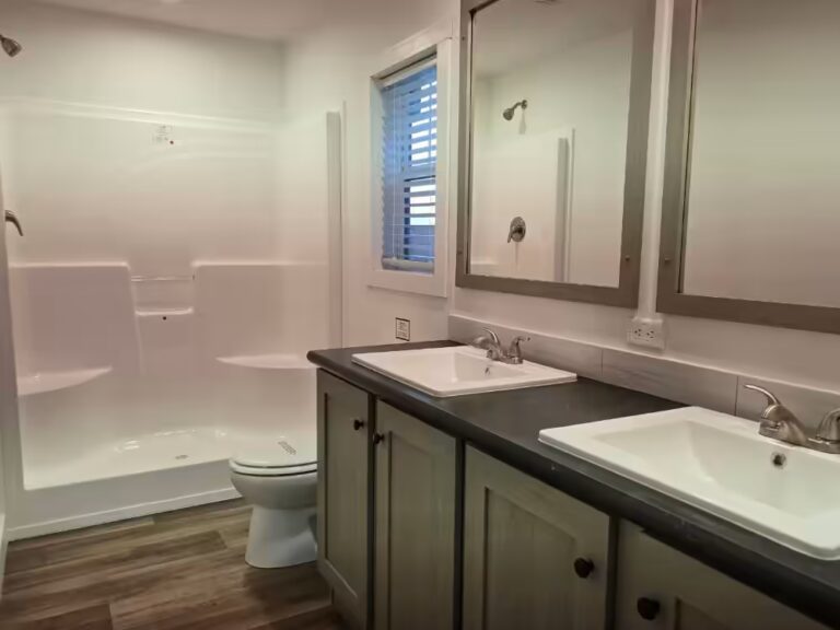Bathroom with walk-in shower, toilet, and double sink vanity with large mirrors and wood flooring.