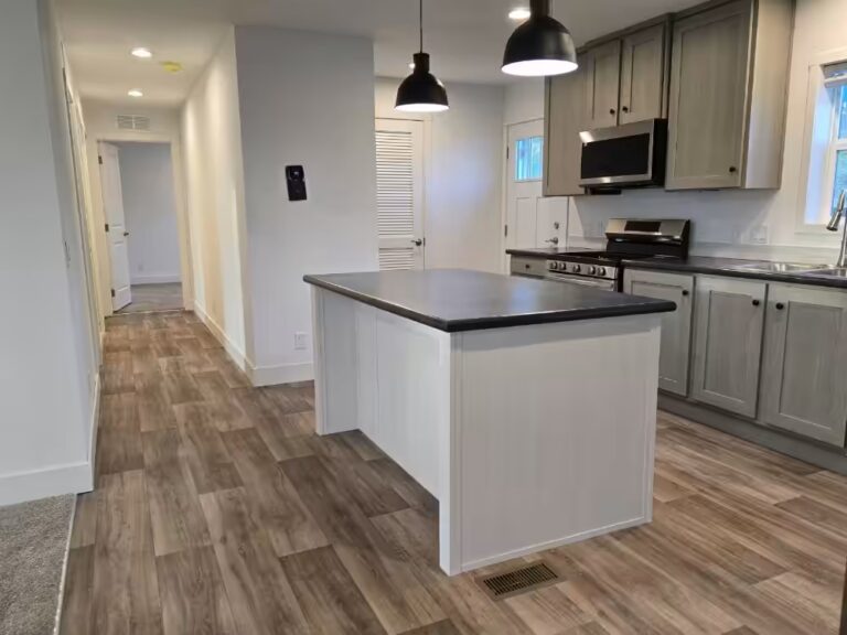Kitchen island with dark countertop under black pendant lights, gray cabinets, wood-look flooring.