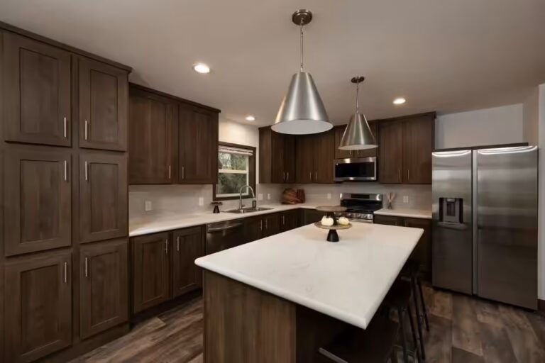 Modern kitchen with dark wood cabinets, white island, pendant lights, stainless steel appliances.