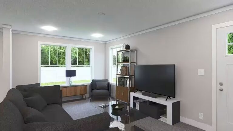 Modern living room with gray sectional sofa, flat-screen TV, and windows overlooking greenery.