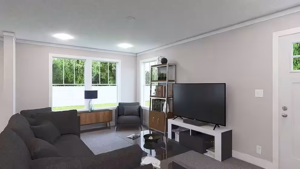 Modern living room with gray sectional sofa, flat-screen TV, and windows overlooking greenery.