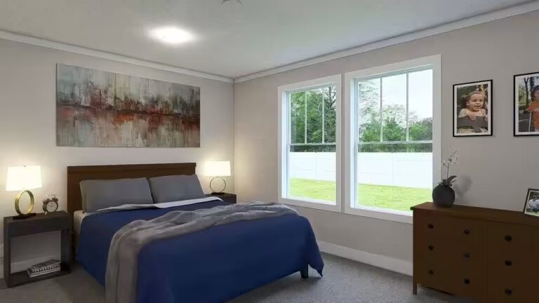 Bedroom with blue bed, table lamps, abstract art, and windows overlooking a fenced green yard.