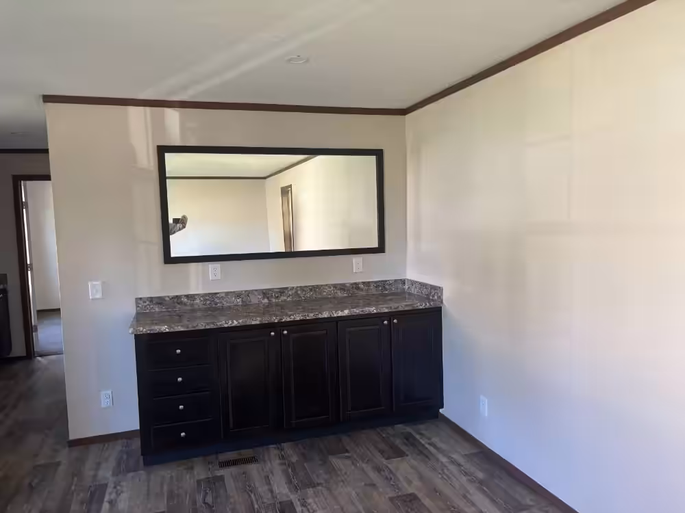 Dark wood vanity with granite countertop and large mirror in an empty room