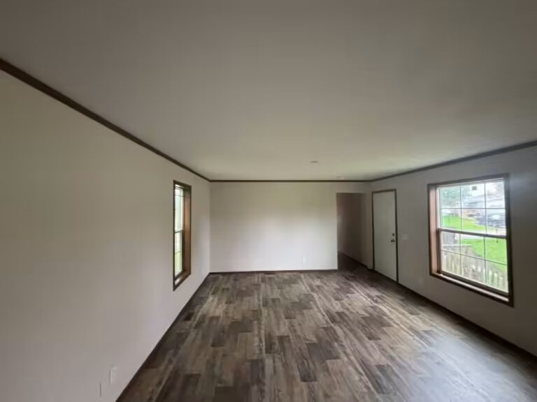 Empty room with wood-look flooring, white walls, two windows, and a closed door.