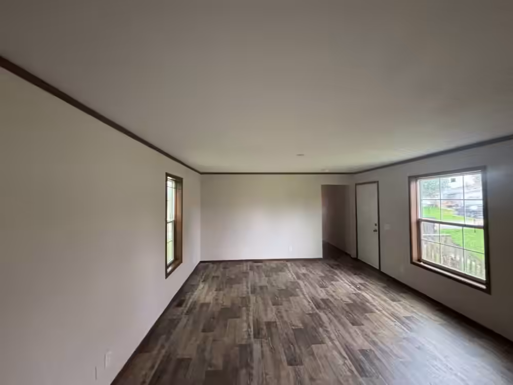 Empty room with wood-look flooring, white walls, two windows, and a closed door.