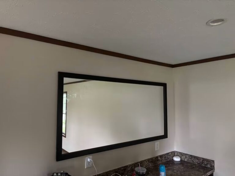 Large rectangular mirror with black frame mounted on beige wall above granite countertop