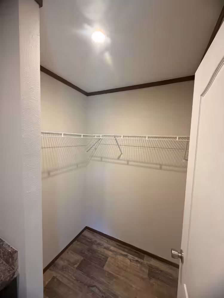 Empty walk-in closet with white wire shelving, beige walls, wood-look floor, and open door.
