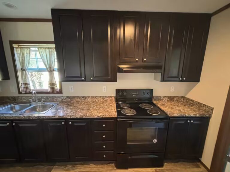 Kitchen with dark cabinets, granite countertops, black electric stove, sink under curtained window