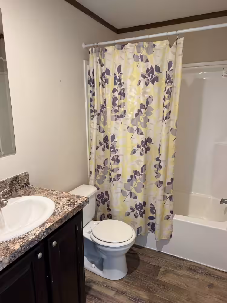 Bathroom with granite vanity, white toilet, and bathtub behind yellow leaf-patterned shower curtain