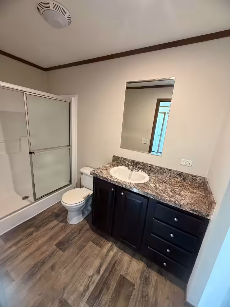 Bathroom with dark wood vanity, granite countertop, mirror, toilet, and glass shower door