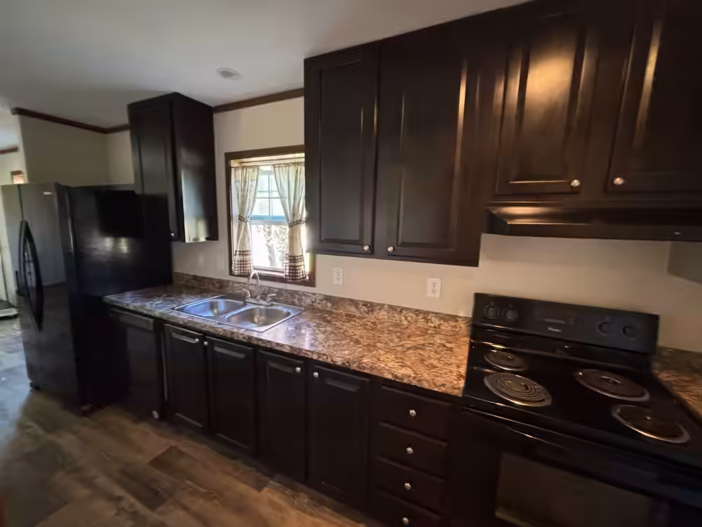 Kitchen with dark cabinets, granite countertops, black appliances, and window over double sink