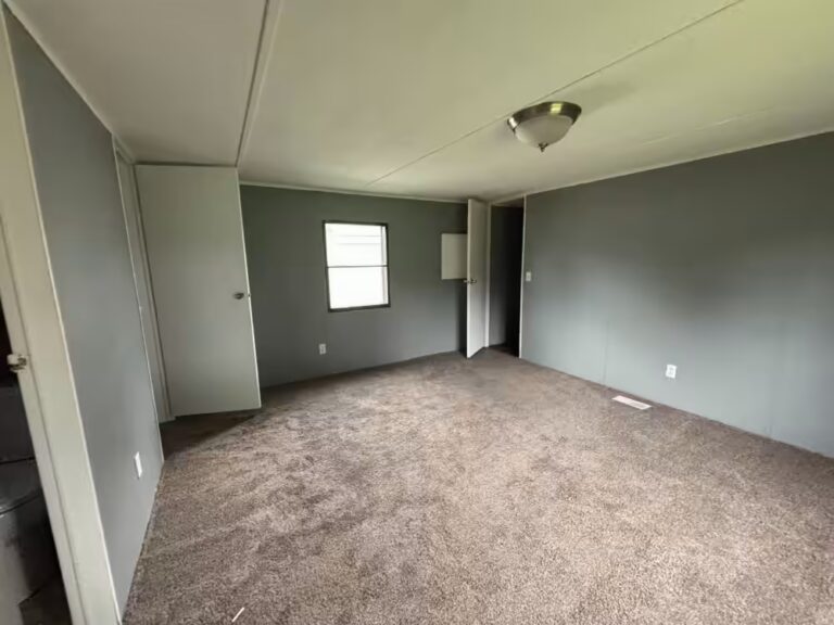 Empty room with gray walls, beige carpet, white door, small window, and ceiling light fixture