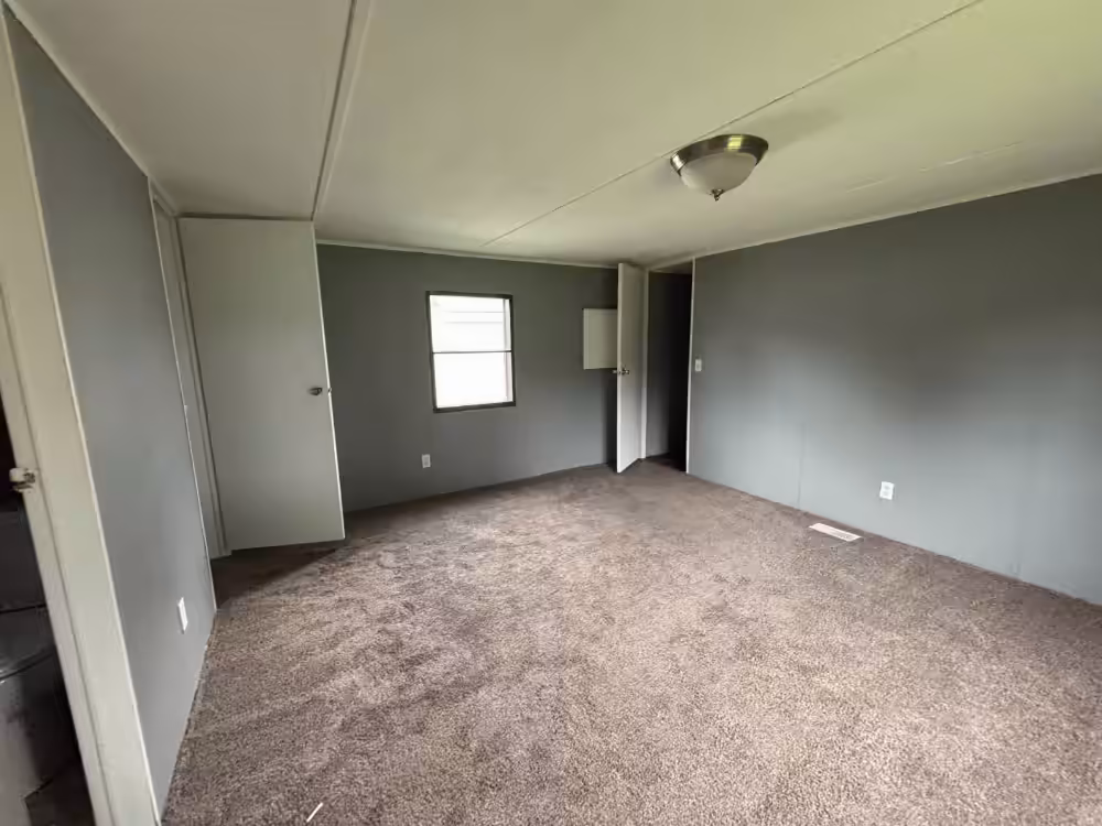 Empty room with gray walls, beige carpet, white door, small window, and ceiling light fixture