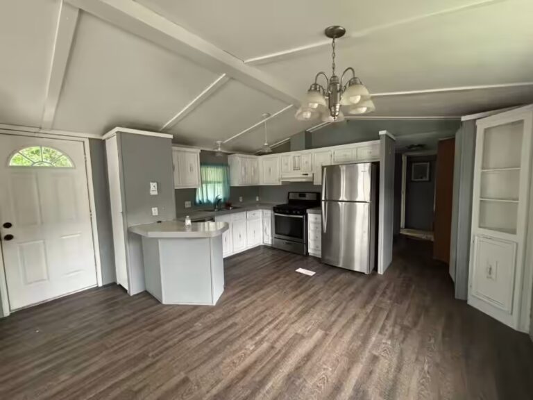 Empty home interior with white kitchen cabinets, stainless steel fridge, and wood-look flooring