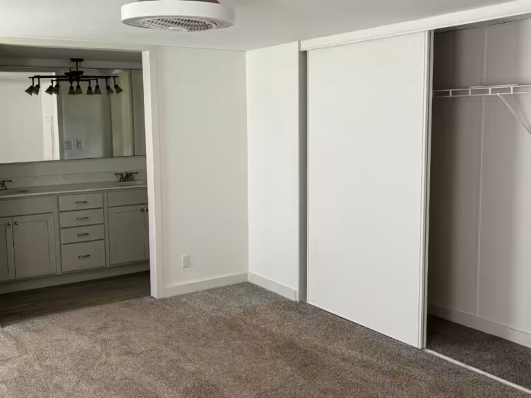 Empty room with carpeted floor, sliding closet doors, and bathroom vanity visible through doorway.