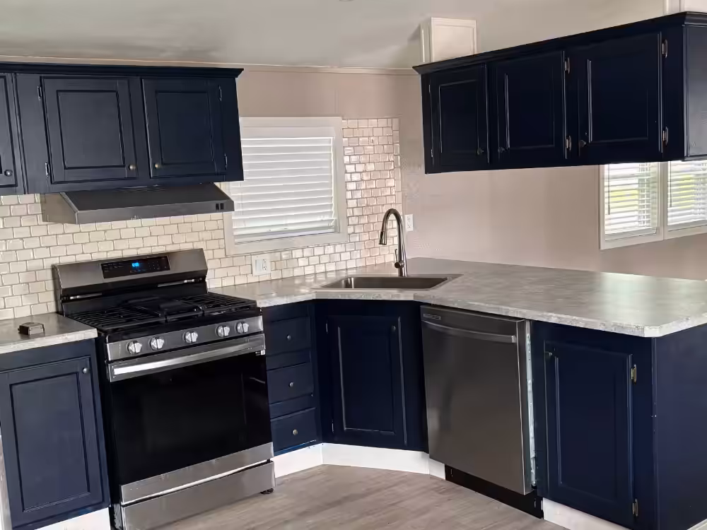 Navy blue kitchen with white subway tile backsplash, stainless gas stove, dishwasher, and marble countertops.