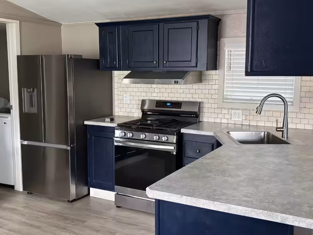 Kitchen with navy cabinets, stainless steel refrigerator and gas stove, gray countertops, and subway tile backsplash.