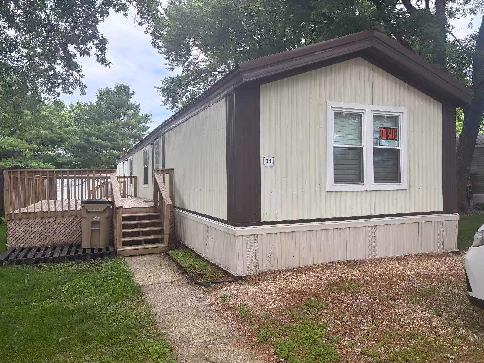 Mobile home with wooden deck and stairs, "FOR SALE" sign in window, house number 34.